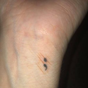 A semicolon tattoo on a wrist.