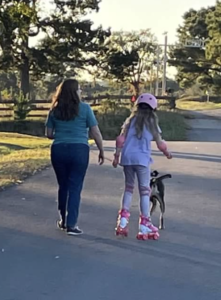 Woman walking with a dog near a girl roller skating.
