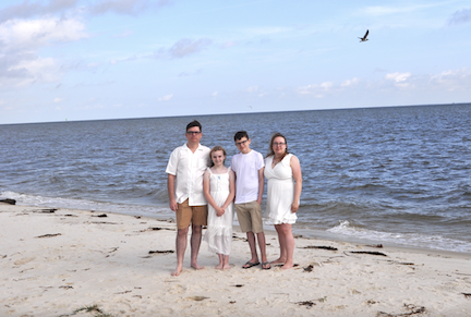Family of four posing on the beach.